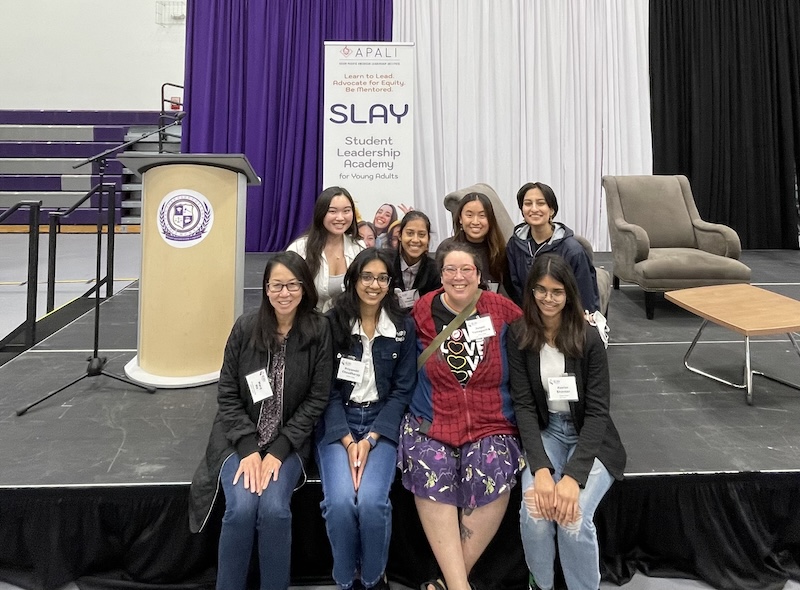 Students and staff sitting on a stage, smiling for a group photo.