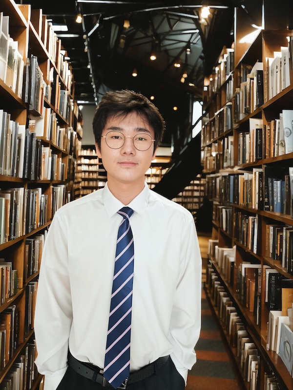 Nathan Tam in a button up shirt and tie standing in a library.