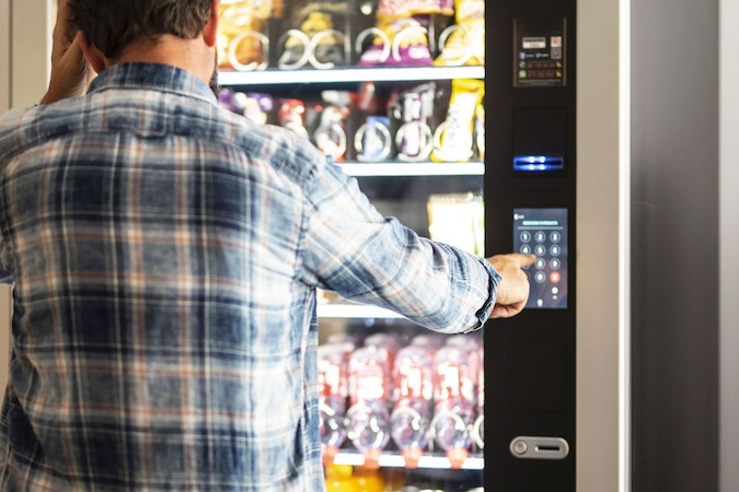 man in a plaid shirt operates a vending machine full of snacks