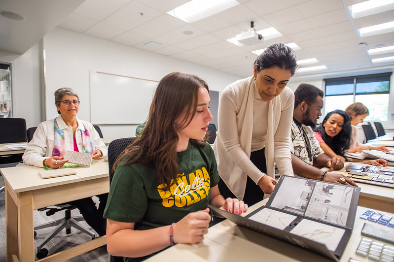 Interior design student reviewing design drawings with instructor standing beside them in a classroom.