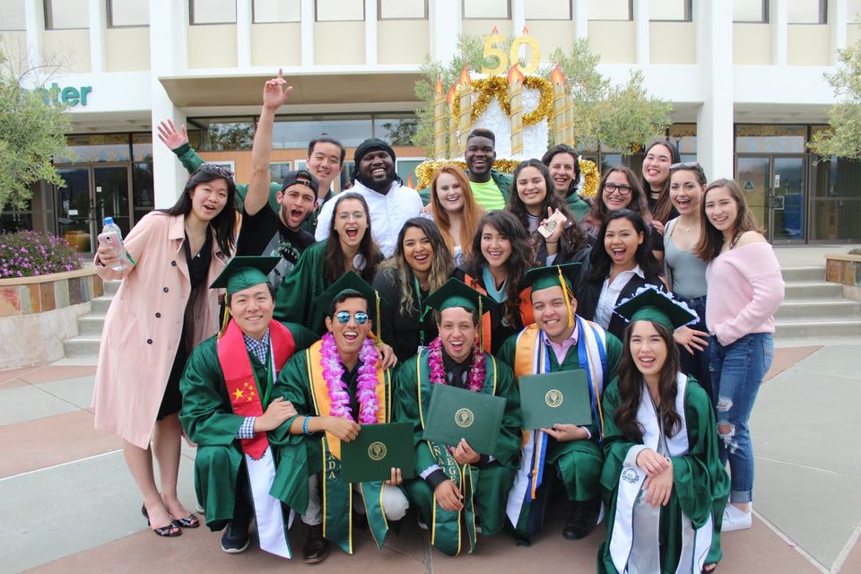 Group of international students graduating pose for a picture while wearing green cap and gowns