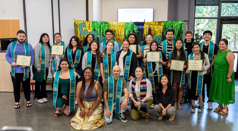 Promise Scholars graduates stand together, wearing sashes and proudly holding their certificates for a group photo.